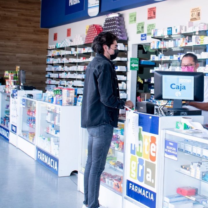 Cliente en la caja de una sucursal de Farmacias Integra, con el mostrador y los anaqueles de medicamento al fondo